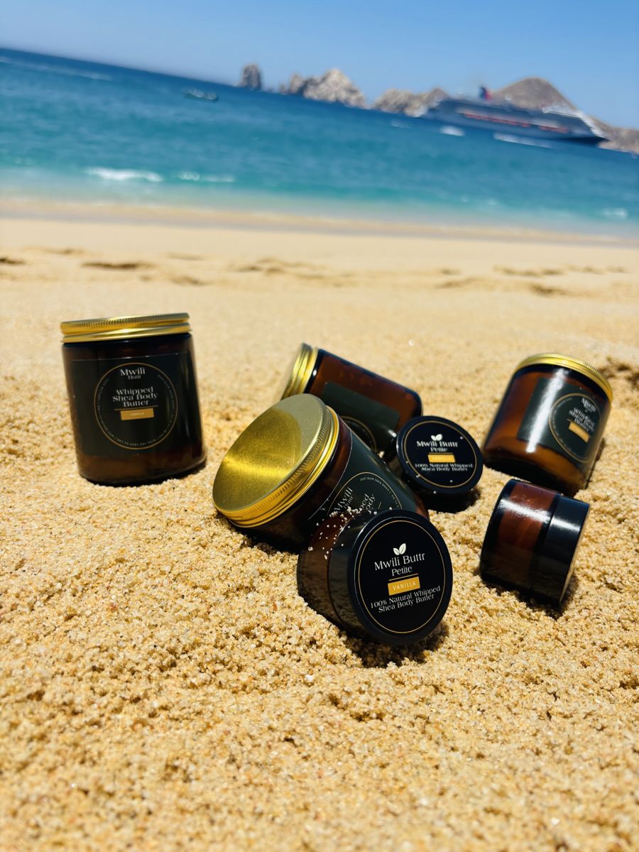 Mwili Buttr jars with gold lids and Mwili Buttr Petite jars with black lids on a sandy beach
